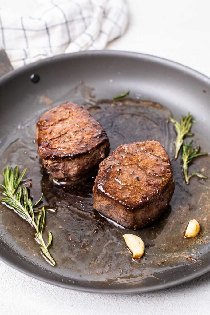 The best way to cook filet mignons shown in cooking two steaks in a cast iron pan.