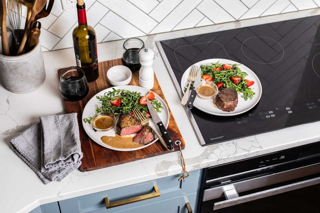 Two plates with filet mignon steaks and a strawberry arugula salad sitting on the sharp induction cooktop.