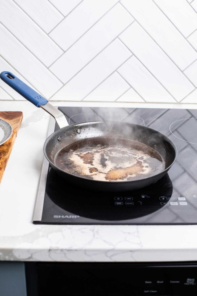 Beef broth added to a skillet with brandy, showing to reduce the liquid by half.