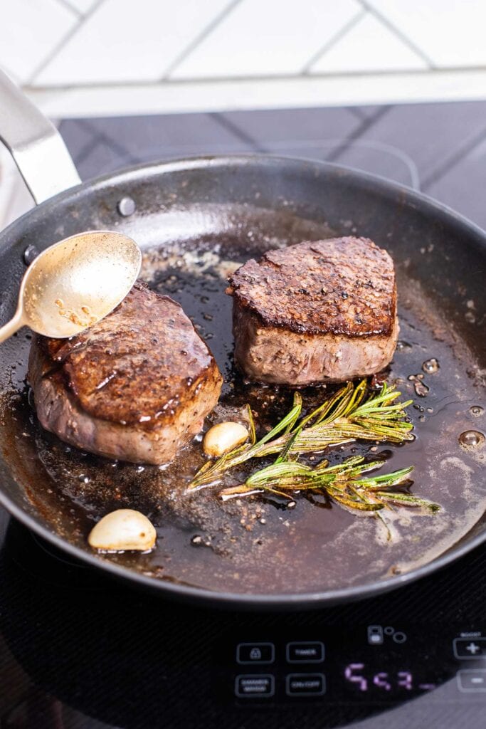 Add garlic cloves and rosemary and baste the steaks with the butter sauce.