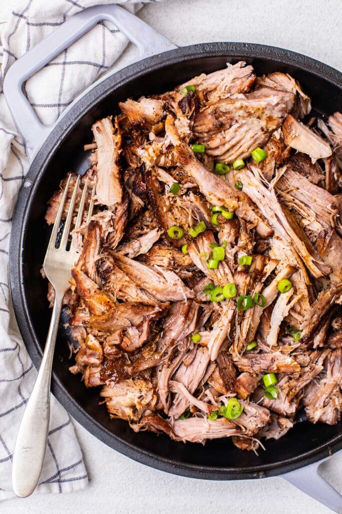 A dish showing pulled pork garnished with green onions with no bbq sauce.