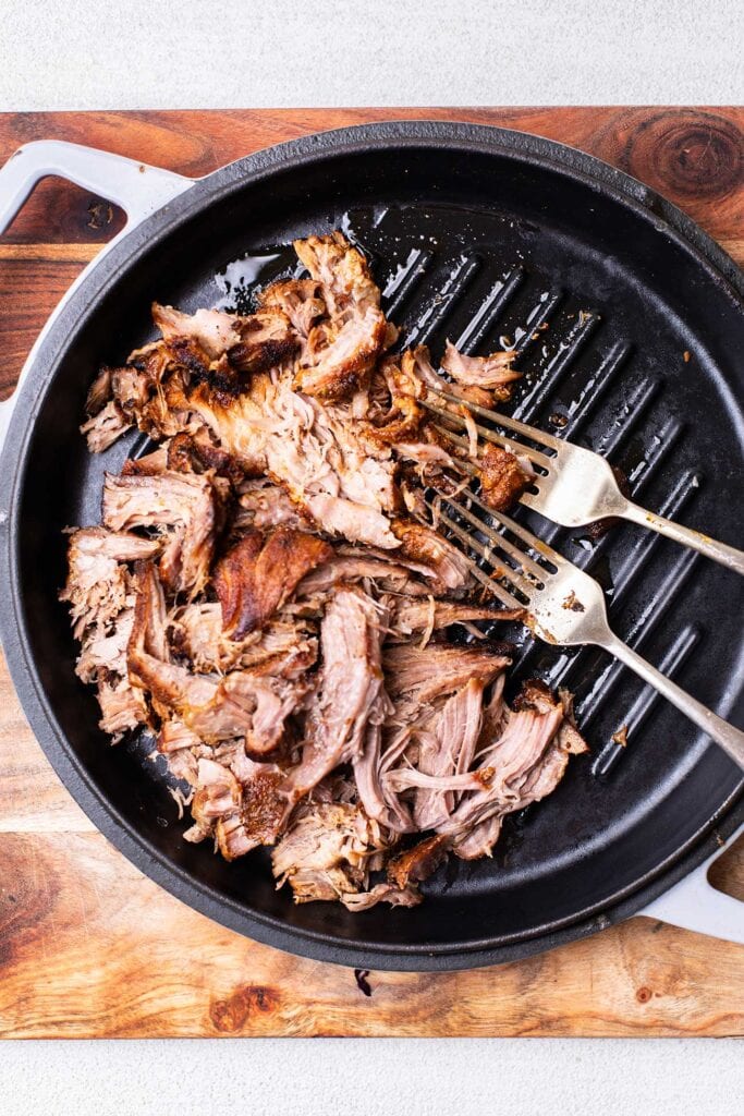 Pork being shredded with two forks.