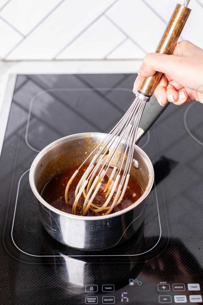 A saucepan with the ingredients for honey bbq sauce recipe being whisked until smooth.