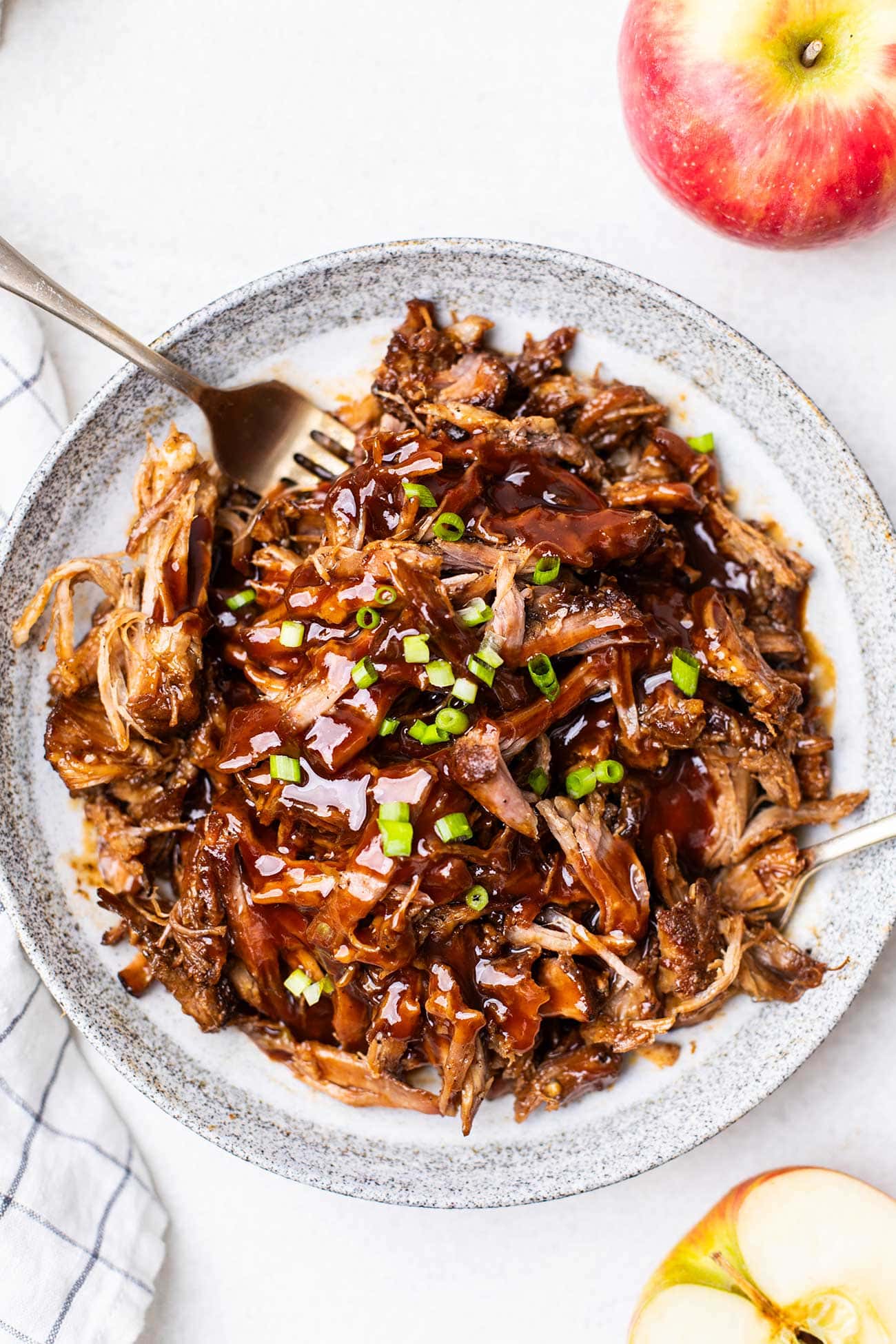 A plate filled with tender pulled pork drizzled with bbq sauce and garnished with green onions.