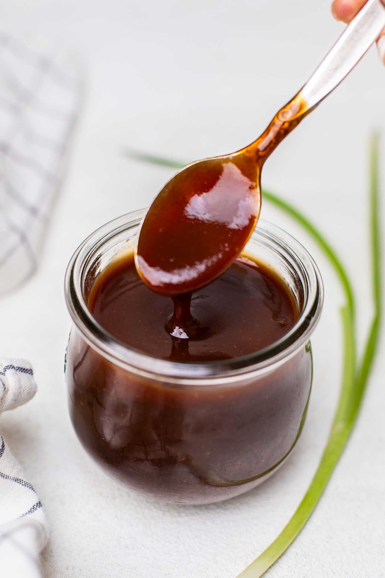 A spoon drizzling some honey bbq sauce out of a jar.