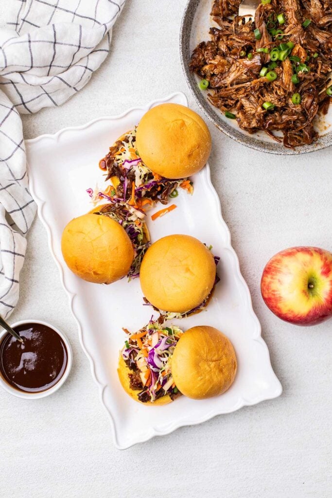 A platter of pulled pork sandwiches with a dish of bbq pulled pork sitting next to it.