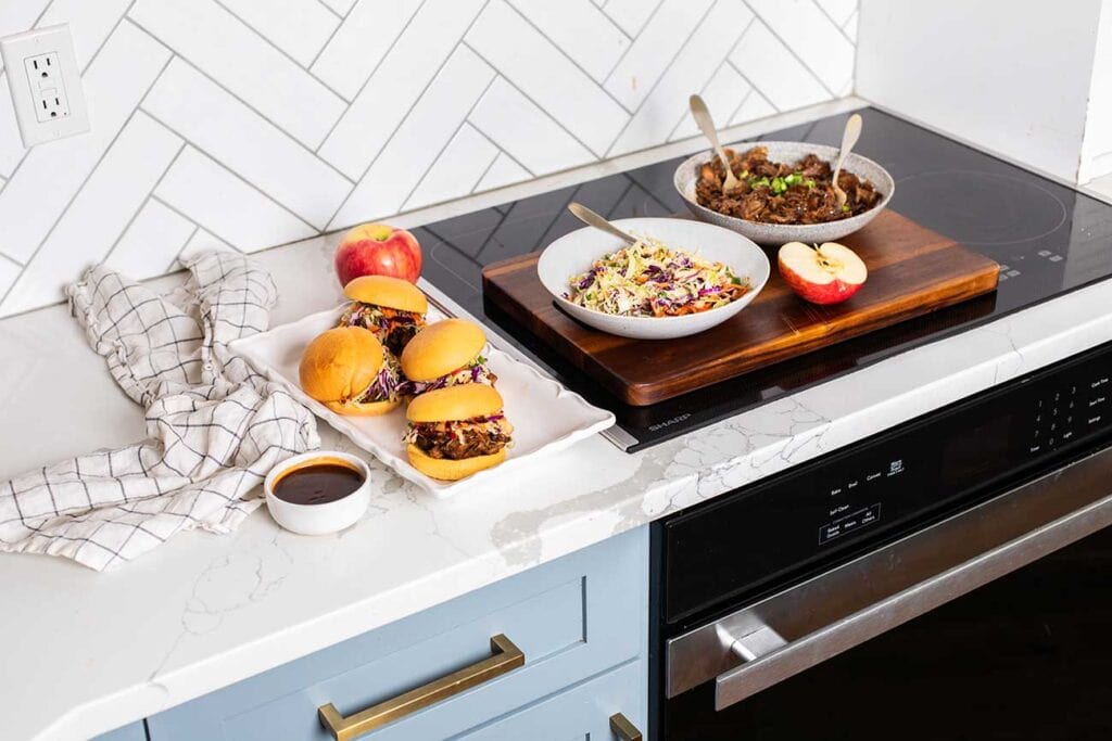 BBQ Pulled pork sandwiches on a platter sitting next to the Sharp Induction Cooktop.