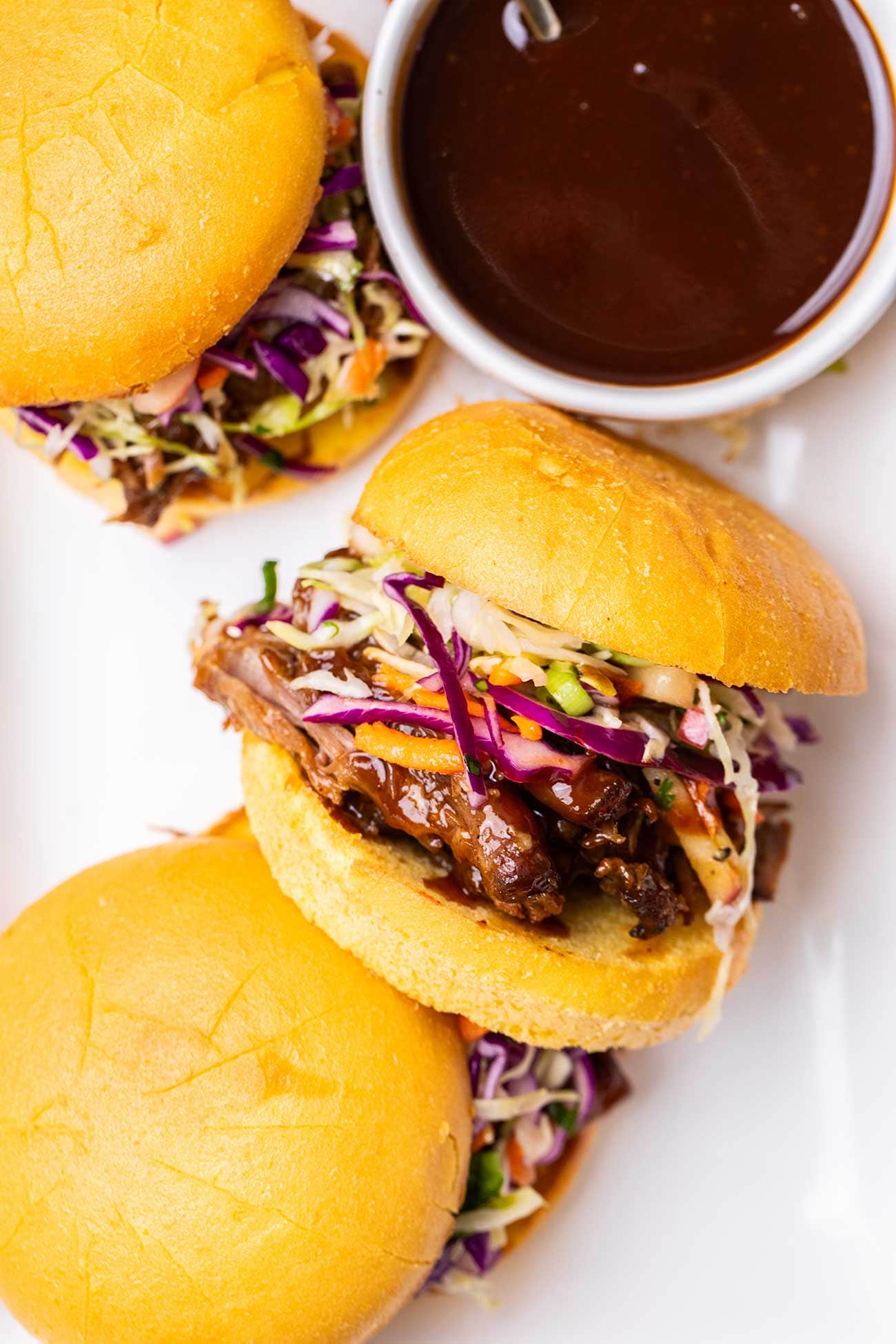 Bbq pulled pork sandwiches sitting on a platter with a ramekin of honey bbq sauce.