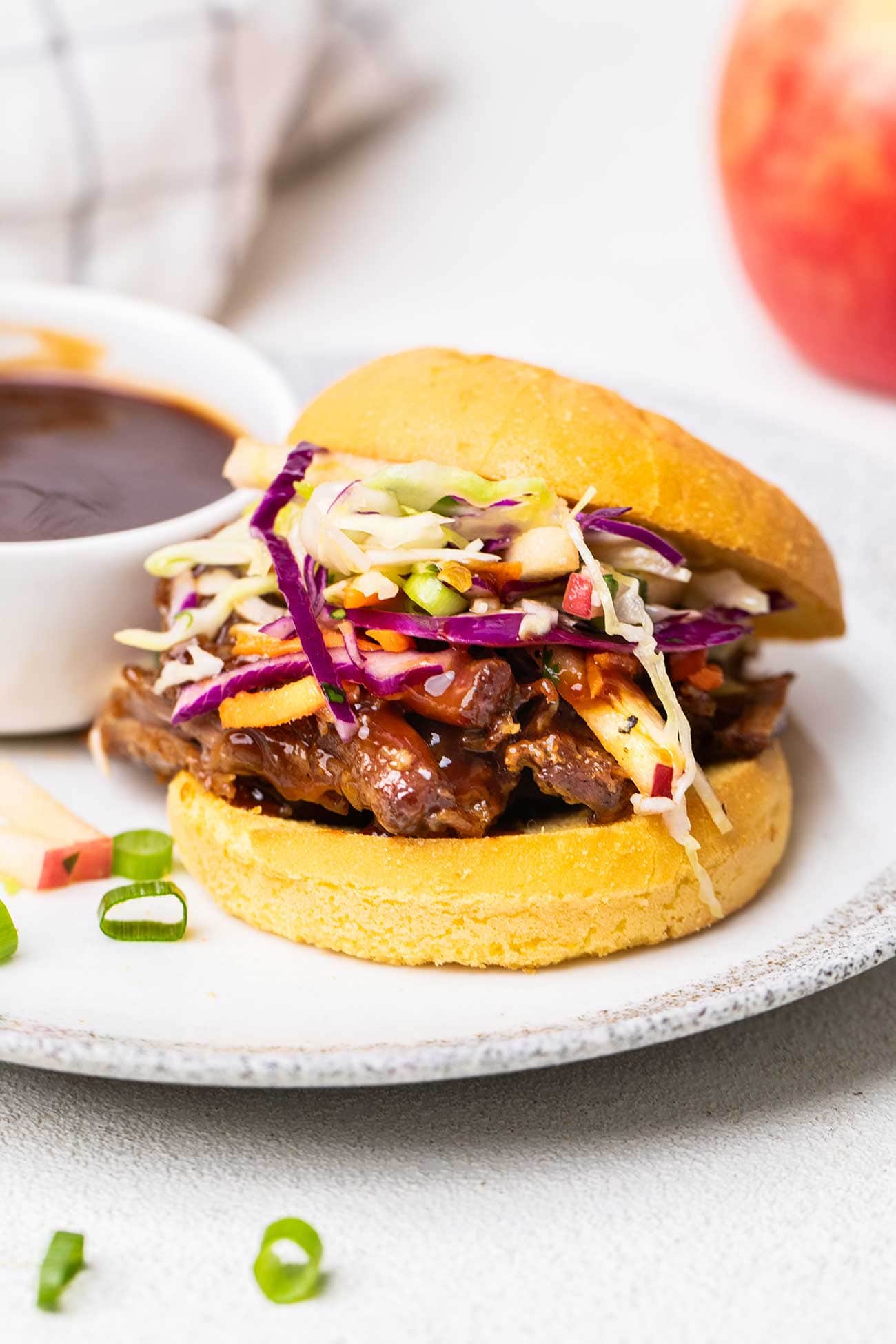 A pulled pork sandwich on a plate with a ramekin of honey bbq sauce.