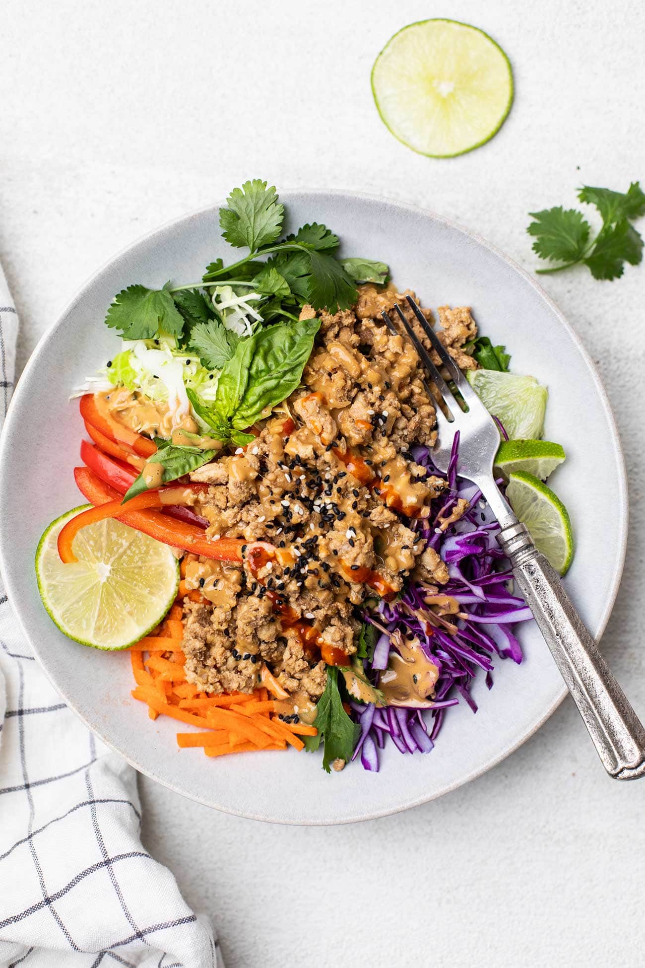 A spring roll salad on a plate loaded with colorful cabbage, carrots, and herbs, topped with spicy chicken.