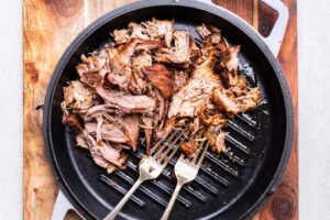 Pork being shredded with two forks.