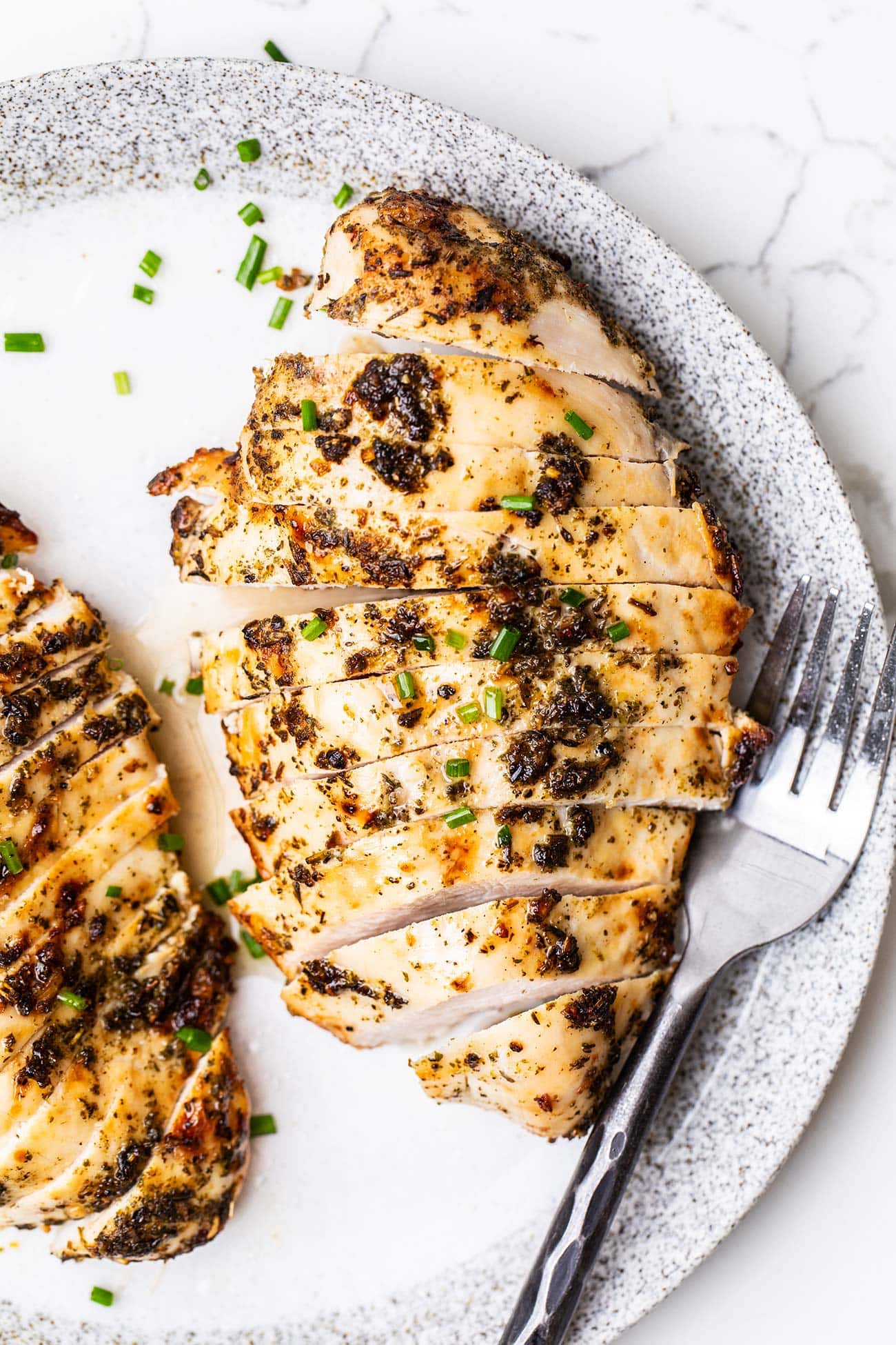 An air fryer chicken breast cut into slices to show how tender the meat is sitting on a white plate.