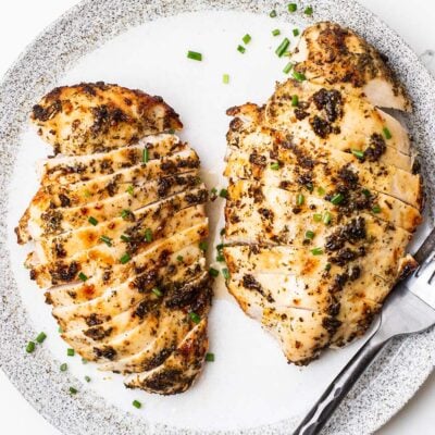 Two air fryer chicken breasts on a plate garnished with chives.