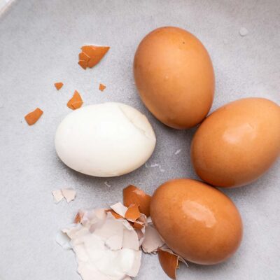 Air Fryer hard boiled eggs shown in a blue bowl being peeled.