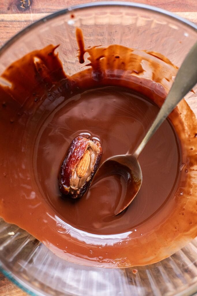 A peanut butter stuffed date shown being rolled in melted chocolate.