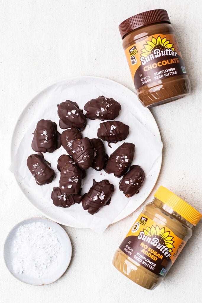 A plate of chocolate dates sitting next to two jars of SunButter.