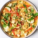 A chicken satay stir fry garnished with fresh herbs in a white cast iron pan.