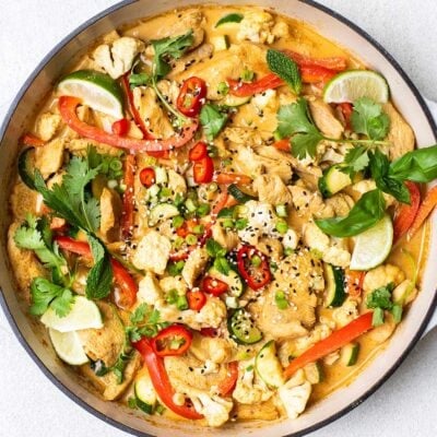 A chicken satay stir fry garnished with fresh herbs in a white cast iron pan.