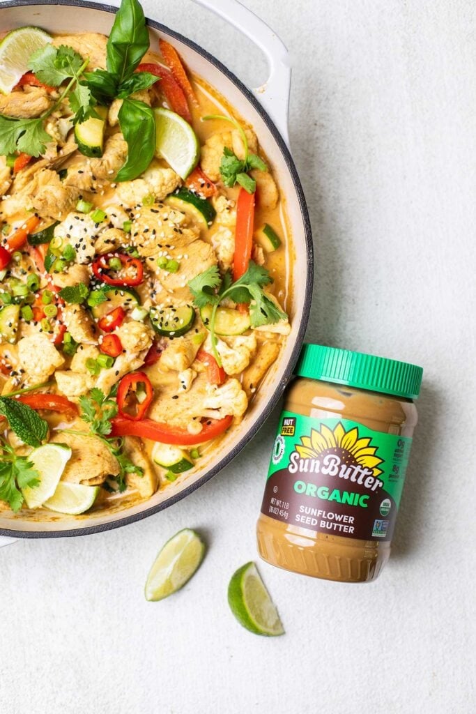 A jar of SunButter sitting next to a skillet of Chicken Satay Stir Fry.