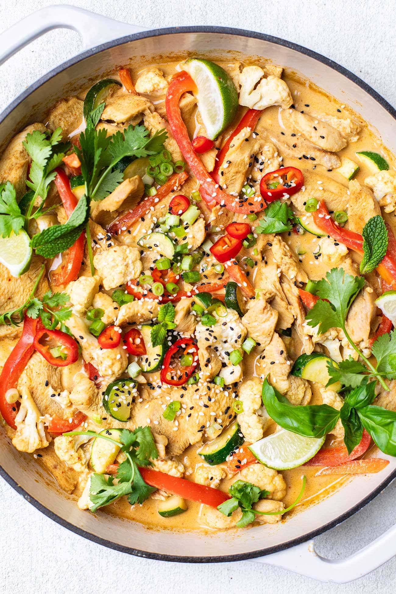 A close up look at chicken and vegetables in a creamy satay sauce in a white cast iron pan.