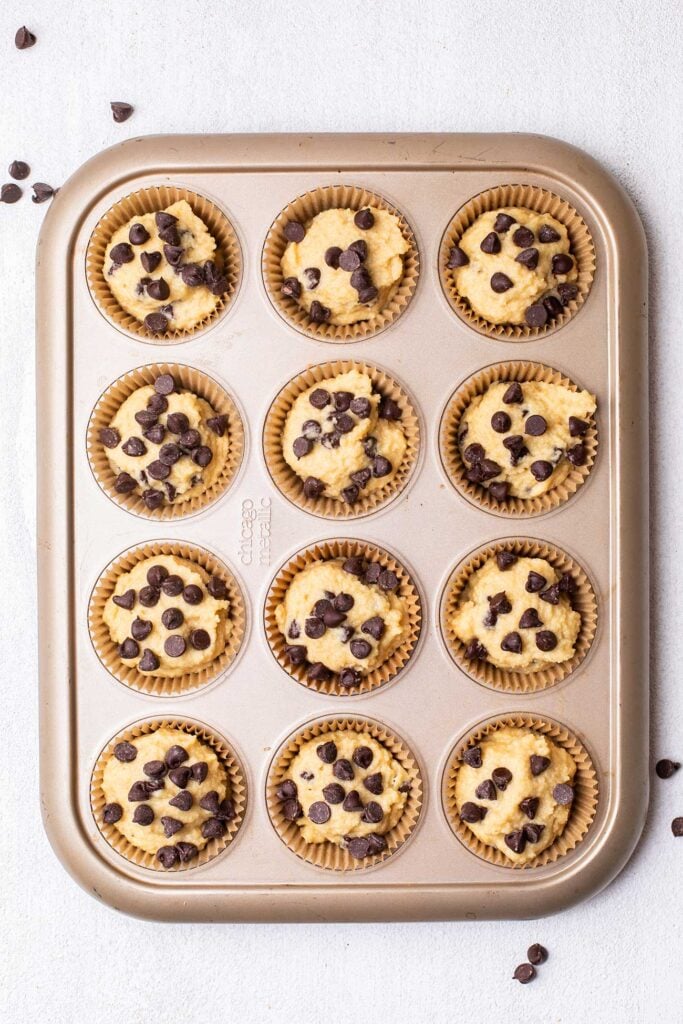 A muffin pan filled with batter and topped with chocolate chips.