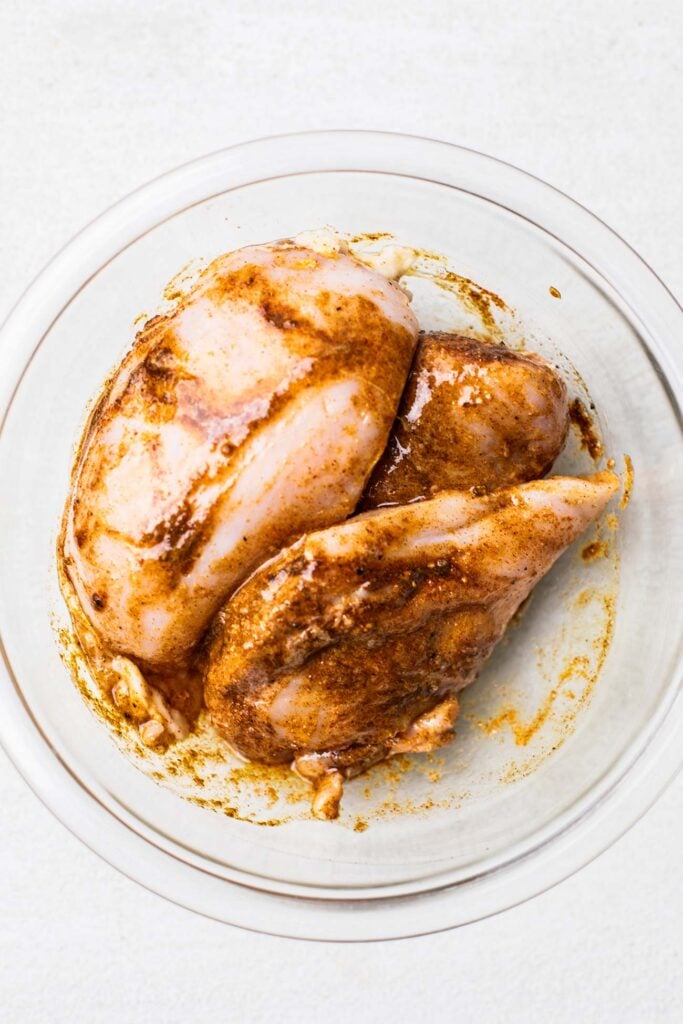 Chicken in a glass bowl shown coated with spices.