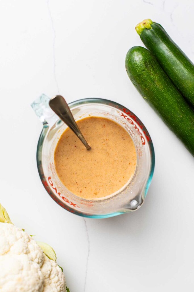 A creamy satay sauce whisked together in a glass measuring cup.