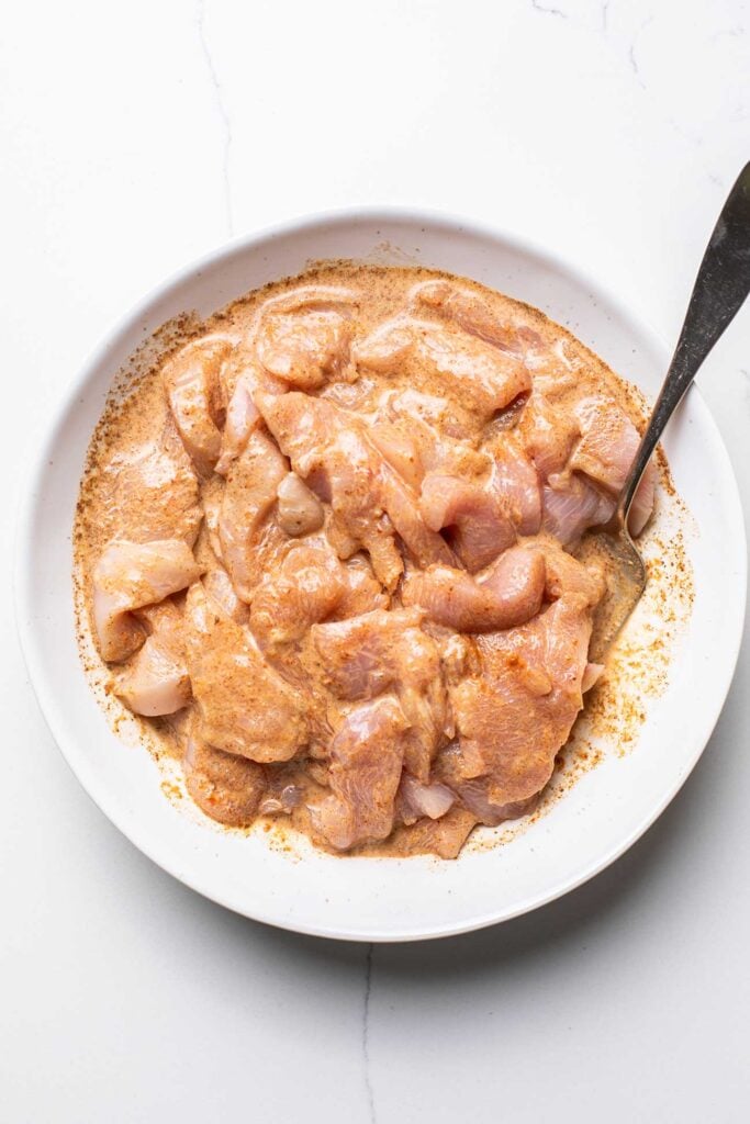Sliced chicken marinating in a creamy sauce.