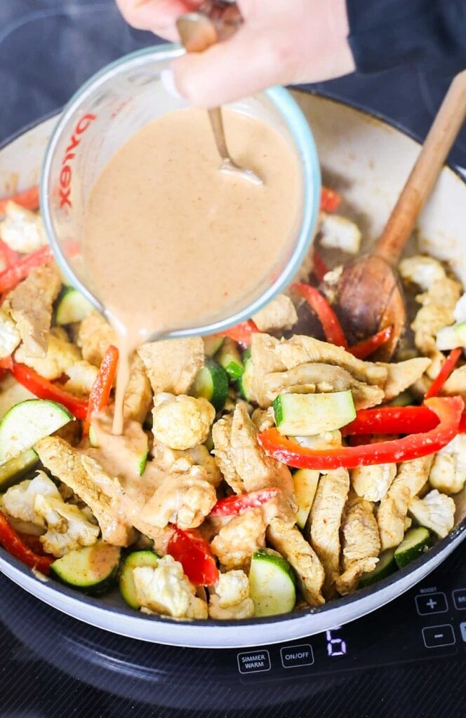 The satay sauce being poured over the chicken and veggies.