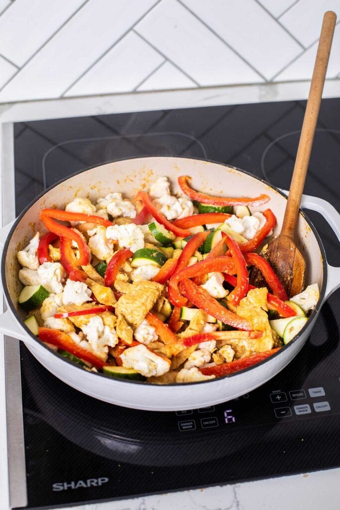 Veggies stir-frying with the chicken in a large skillet.