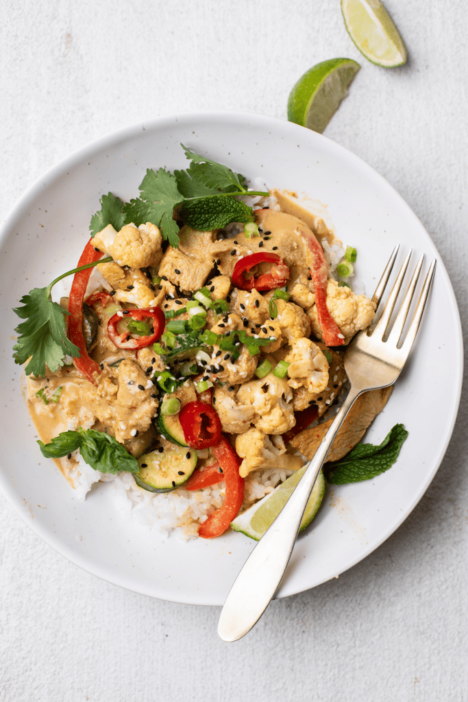 Satay stir fry served over rice with lime wedges.