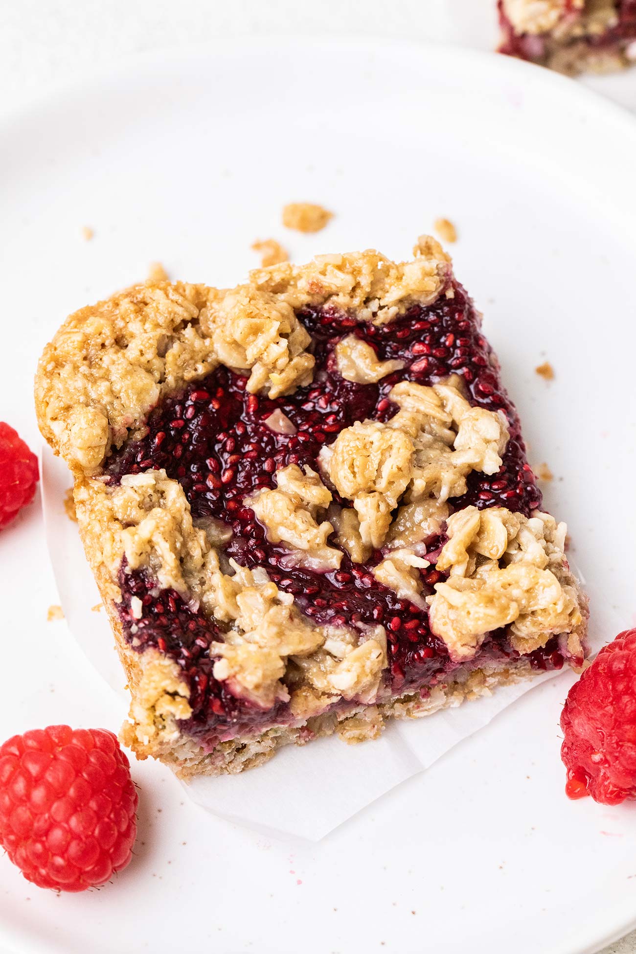 A raspberry bar on a white plate with a few raspberries surrounding it.