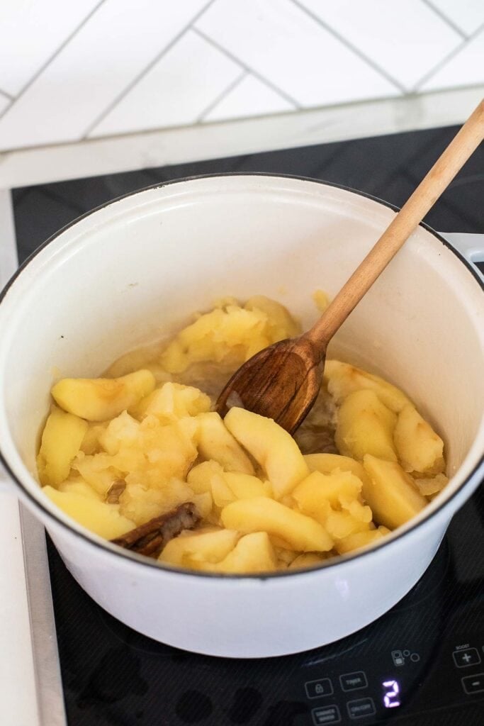 Apples in a pot being stirred with a wooden spoon.