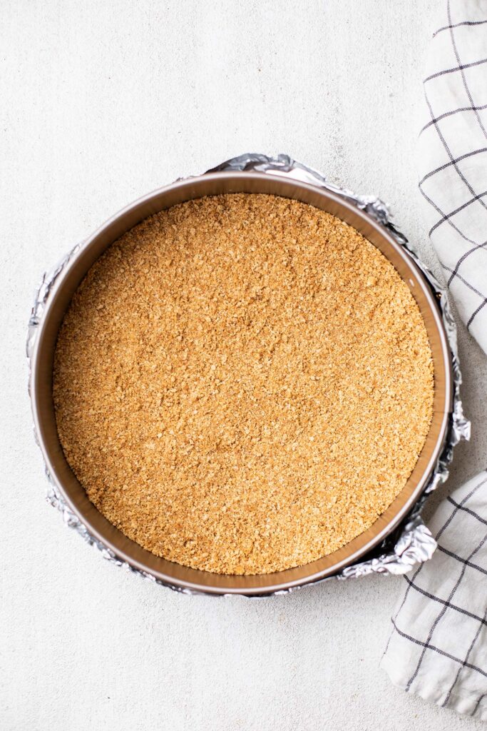 Graham cracker crumbs pressed into the bottom of a springform pan to form a crust.