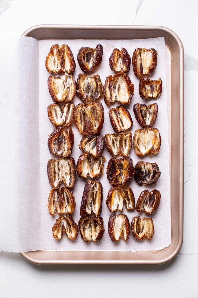 Dates cut in half and laid out in a rectangle shape on the parchment paper.