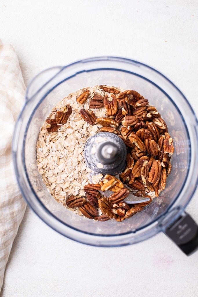Oats and pecans in a food processor bowl.