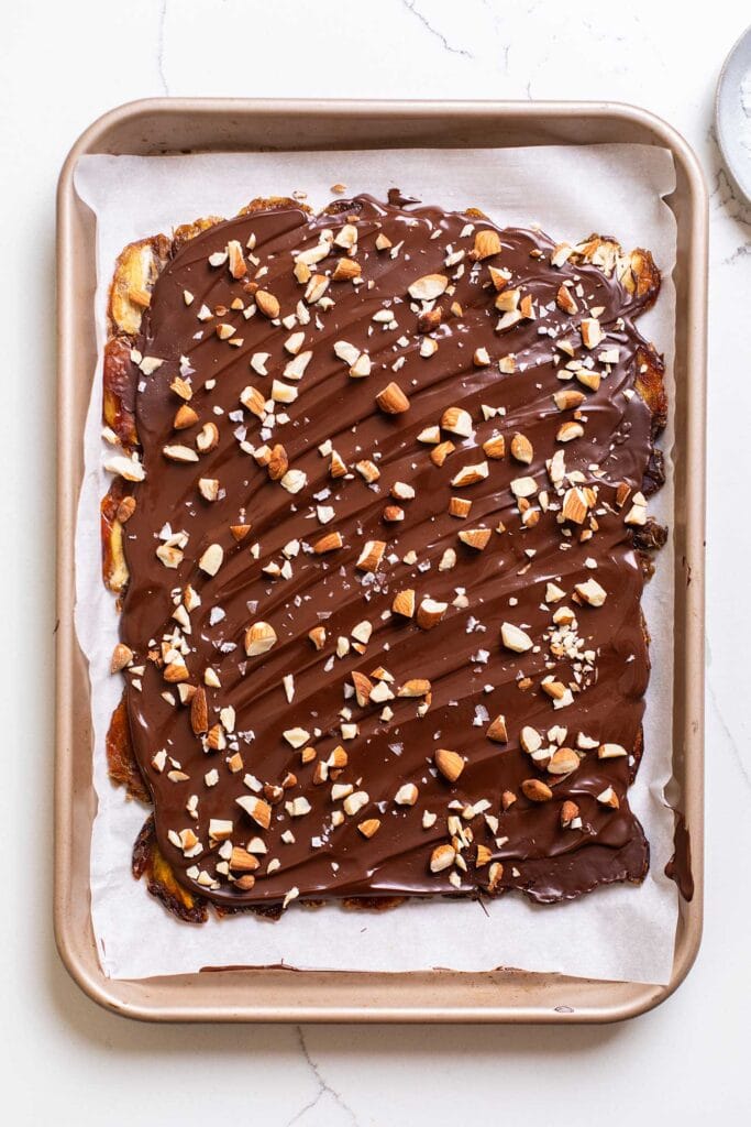 Dates rolled flat and coated with chocolate and sprinkled with chopped almonds.