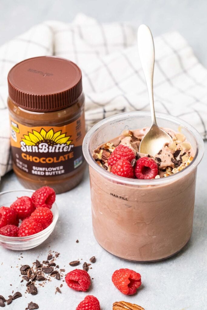 A pint of chocolate protein ice cream next to a jar of chocolate sunbutter.