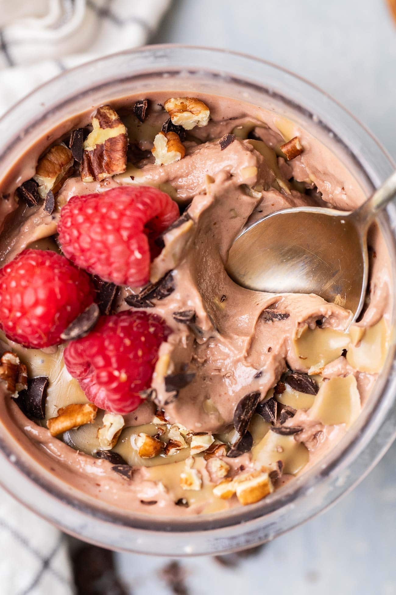 A top down view of a pint of thick chocolate protein ice cream topped with raspberries.