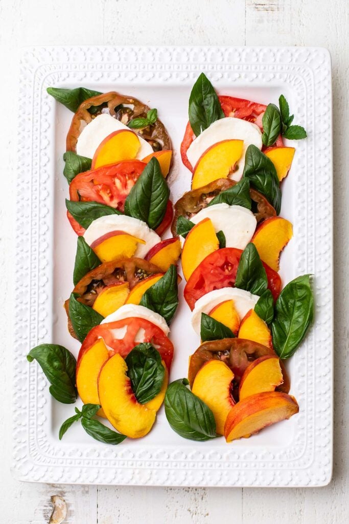 Peaches, tomatoes, mozzarella cheese, and basil leaves layered on a platter.