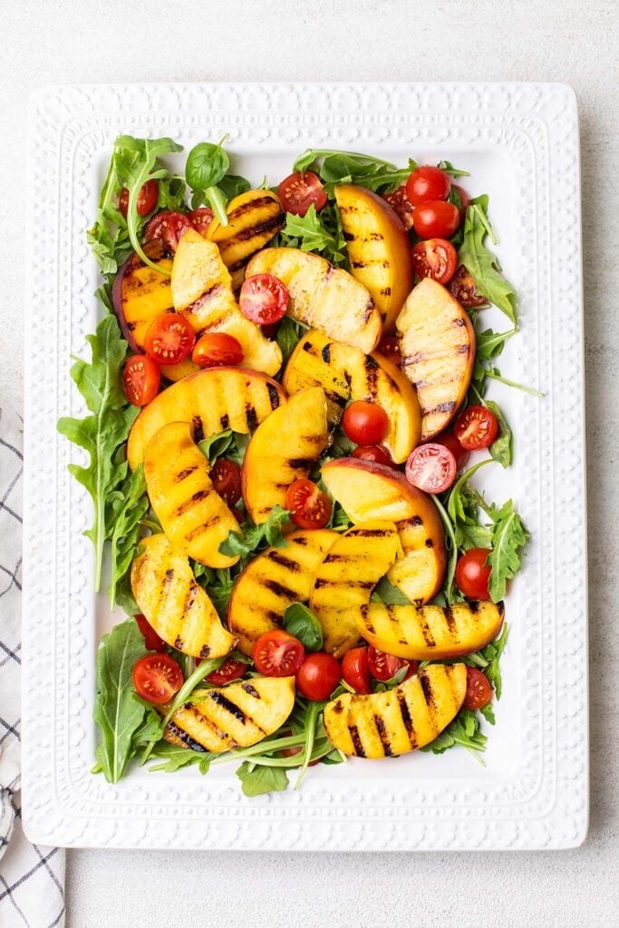 A platter shown with arugula, grilled peaches, and cherry tomatoes.