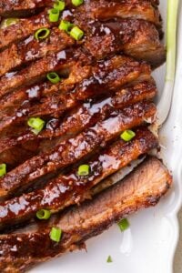A sliced baked beef brisket shown on a white platter.