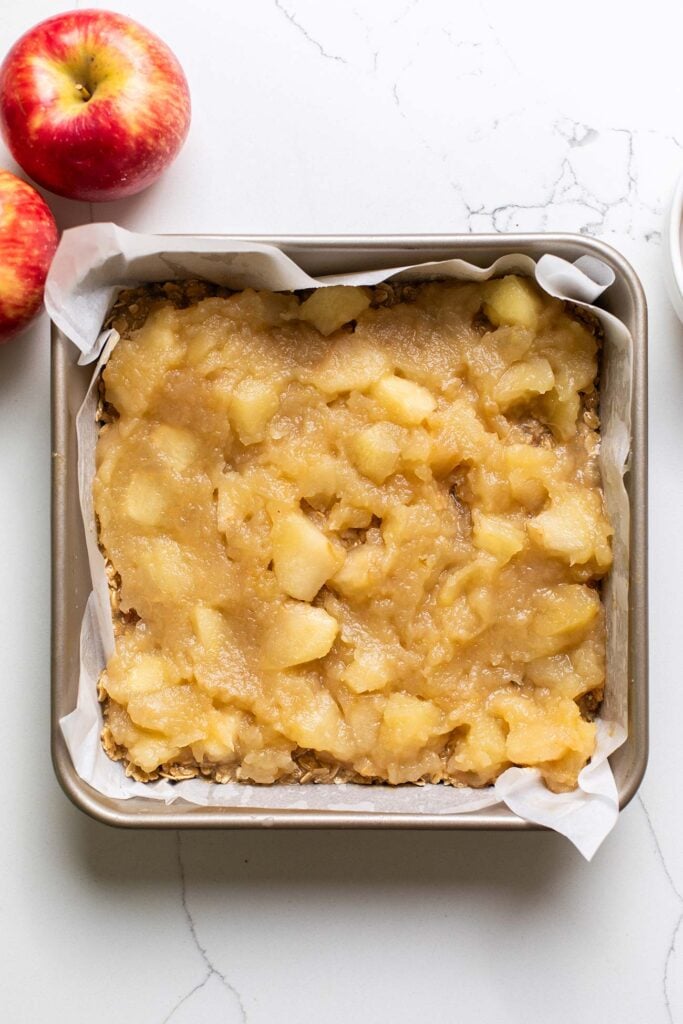 Chunky applesauce spread over the oatmeal layer in the baking pan.