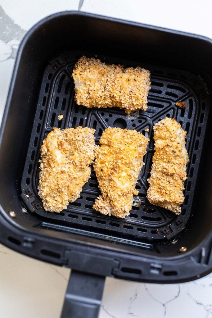 Golden brown crispy cod shown in an air fryer basket.