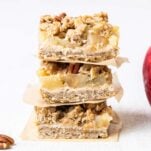 Three applesauce oat cookies shown stacked in front of an apple.