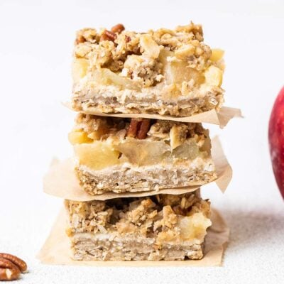 Three applesauce oat cookies shown stacked in front of an apple.