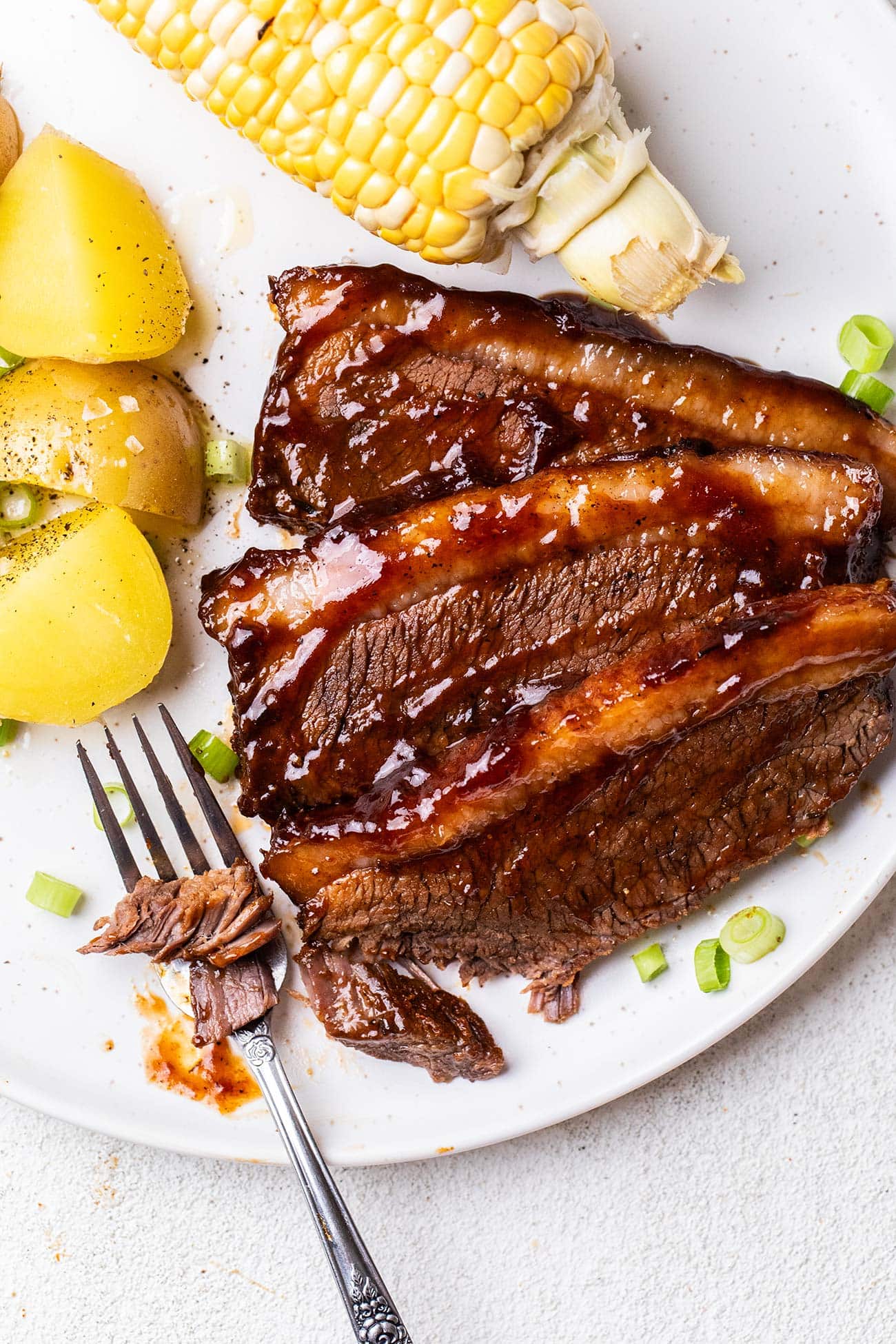 Brisket on a plate with potatoes and corn.