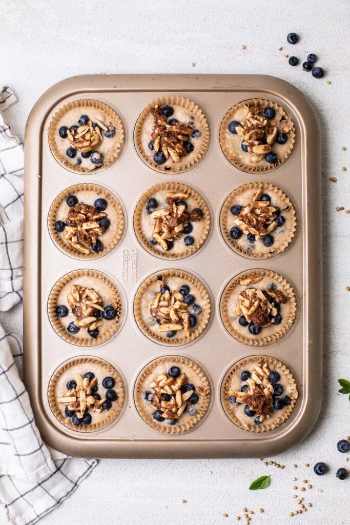 A muffin pan shown with buckwheat muffin batter topped with a streusel topping.