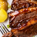 Sliced oven baked brisket shown covered in bbq sauce.