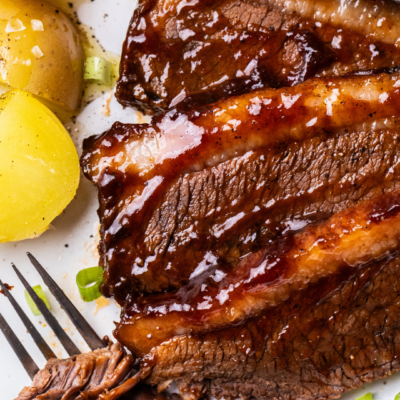 Sliced oven baked brisket shown covered in bbq sauce.